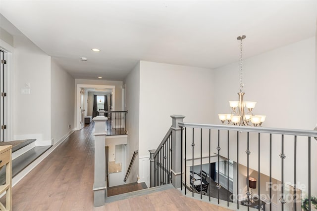 hall with an upstairs landing, a chandelier, wood finished floors, recessed lighting, and baseboards