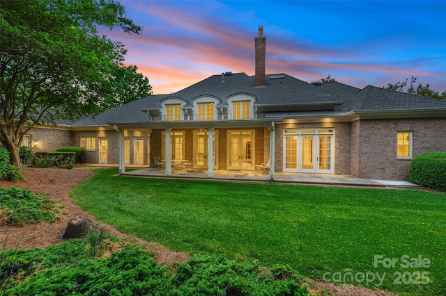5701 Challisford Ln, Charlotte, NC 28226 - back of property at dusk with french doors, brick siding, a shingled roof, a patio area, and a yard