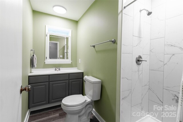 bathroom featuring vanity, toilet, baseboards, wood finished floors, and tiled shower