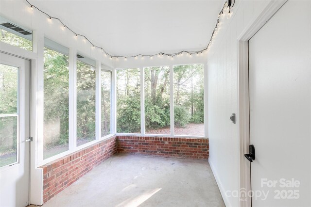 unfurnished sunroom featuring brick wall, visible vents, unfinished concrete flooring, and plenty of natural light