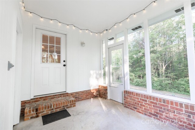 unfurnished sunroom featuring concrete floors, brick wall, and visible vents