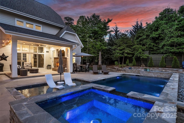 pool at dusk with an in ground hot tub, a fenced in pool, fence, and a patio