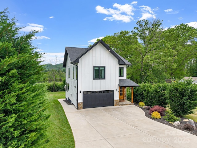 view of side of home with board and batten siding, roof with shingles, concrete driveway, an attached garage, and stone siding
