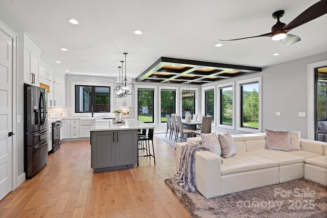 living room featuring beam ceiling, recessed lighting, light wood-type flooring, coffered ceiling, and ceiling fan with notable chandelier
