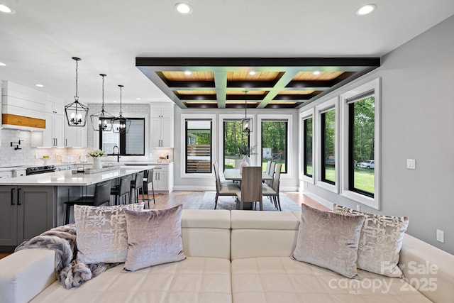 living area with coffered ceiling, recessed lighting, beam ceiling, and a chandelier