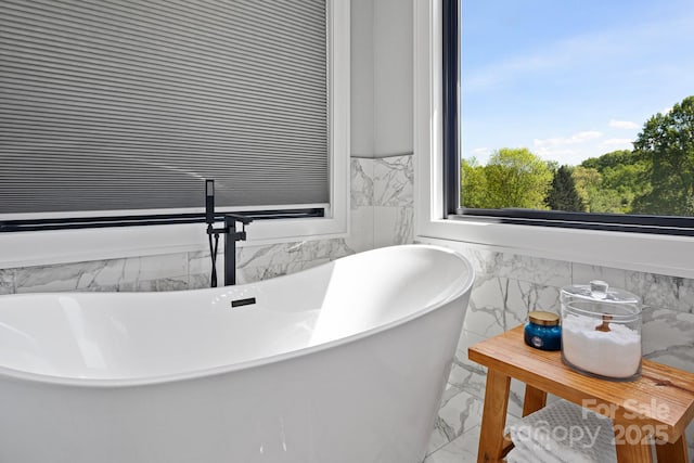 full bathroom featuring tile walls, a wainscoted wall, marble finish floor, and a freestanding bath