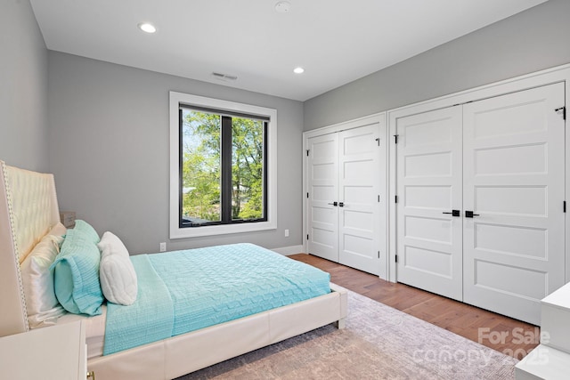 bedroom featuring two closets, recessed lighting, visible vents, and wood finished floors