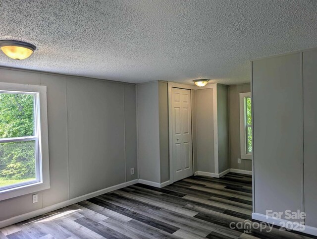 unfurnished room with a textured ceiling, plenty of natural light, baseboards, and wood finished floors