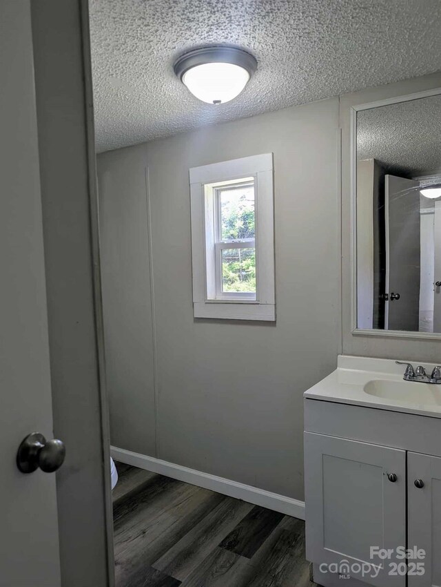 bathroom with vanity, baseboards, a textured ceiling, and wood finished floors
