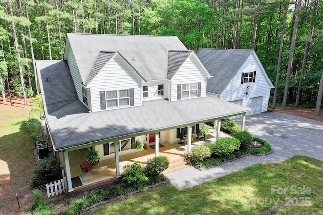 view of front facade featuring a porch, an outbuilding, a detached garage, a wooded view, and driveway