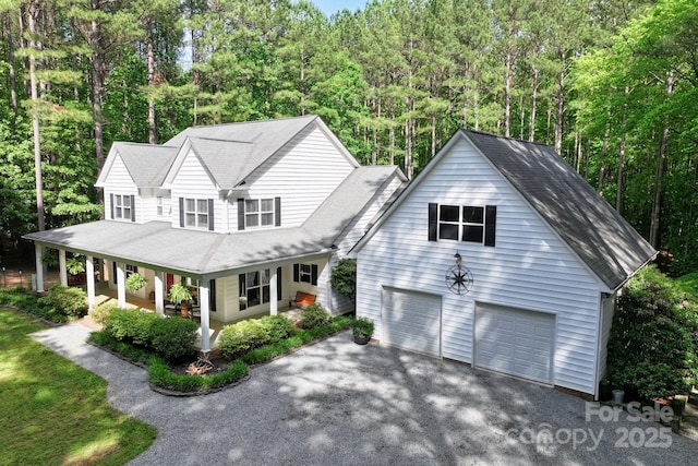 view of front of home with a porch, a garage, asphalt driveway, and a wooded view