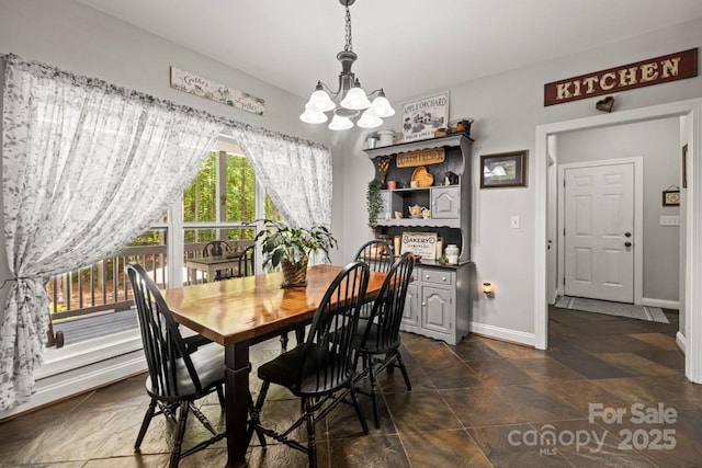 dining room with a chandelier, baseboards, and dark stone finish floors