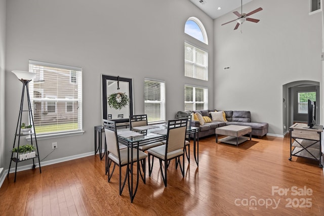 dining room with a ceiling fan, baseboards, high vaulted ceiling, hardwood / wood-style flooring, and arched walkways