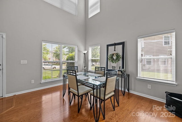 dining space with baseboards, wood finished floors, and a towering ceiling