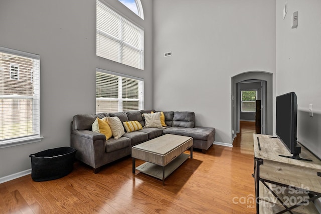 living area with arched walkways, light wood-style flooring, and a towering ceiling