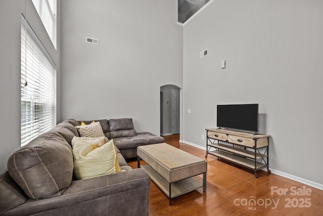 living room with visible vents, arched walkways, baseboards, and a high ceiling