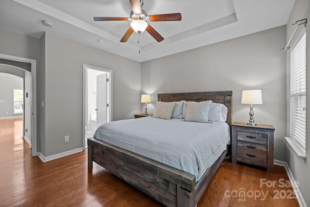 bedroom with arched walkways, multiple windows, a tray ceiling, and wood finished floors