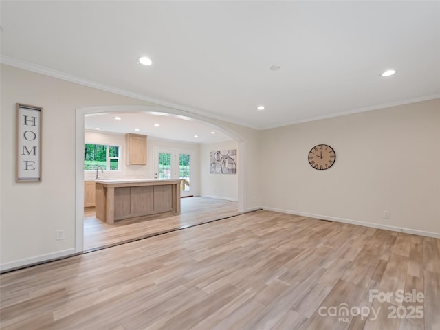 unfurnished living room featuring arched walkways, a sink, ornamental molding, recessed lighting, and light wood-style flooring