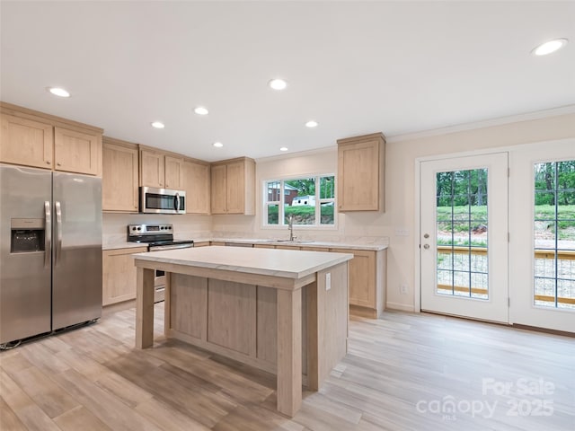 kitchen with light brown cabinetry, light countertops, ornamental molding, stainless steel appliances, and light wood-style flooring