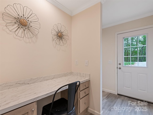unfurnished office featuring baseboards, ornamental molding, light wood-type flooring, and built in desk