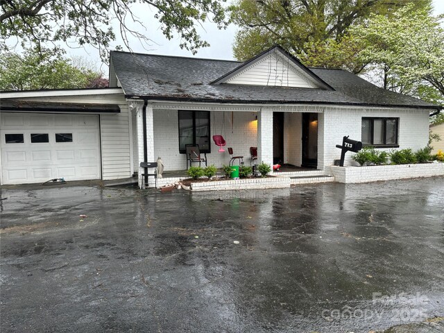 view of front of home with a porch, brick siding, a shingled roof, and a garage