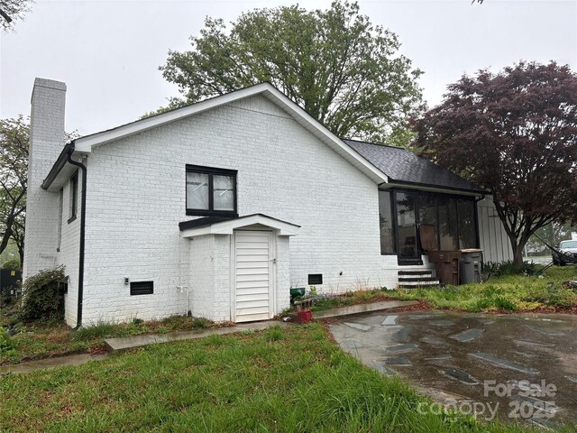 back of property featuring brick siding, a sunroom, a chimney, and entry steps