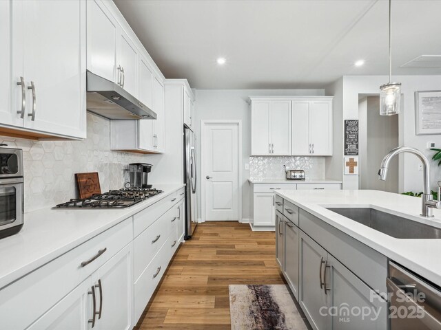 kitchen with appliances with stainless steel finishes, a sink, light countertops, under cabinet range hood, and recessed lighting