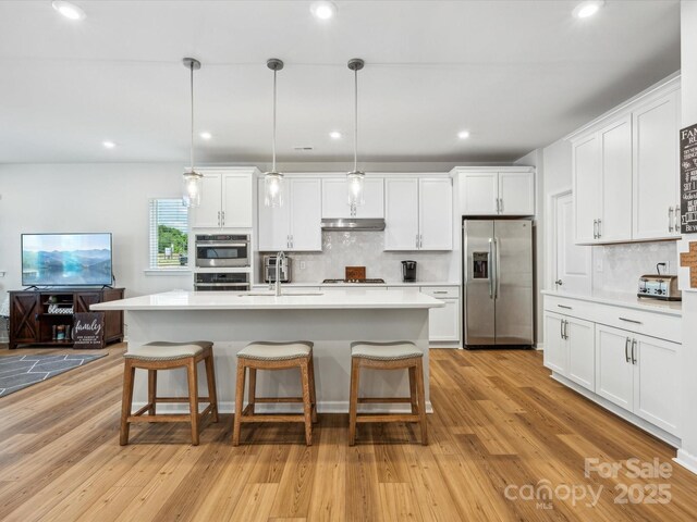 kitchen with appliances with stainless steel finishes, tasteful backsplash, light countertops, a kitchen bar, and under cabinet range hood