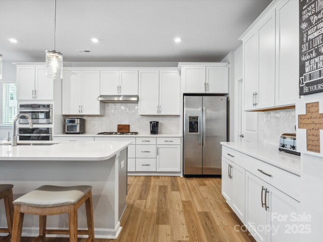 kitchen with appliances with stainless steel finishes, a sink, light countertops, white cabinets, and under cabinet range hood