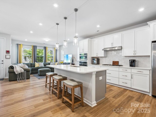 kitchen featuring a breakfast bar, a sink, light wood finished floors, open floor plan, and under cabinet range hood