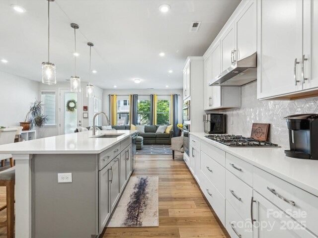 kitchen featuring open floor plan, under cabinet range hood, a sink, gray cabinetry, and stainless steel appliances