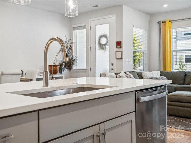 kitchen with a sink, light countertops, plenty of natural light, open floor plan, and stainless steel dishwasher