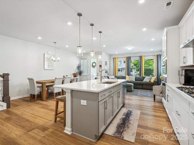 kitchen with gray cabinetry, light countertops, a sink, open floor plan, and stainless steel appliances