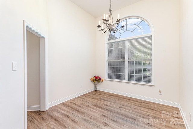 unfurnished room featuring a chandelier, wood finished floors, vaulted ceiling, and baseboards