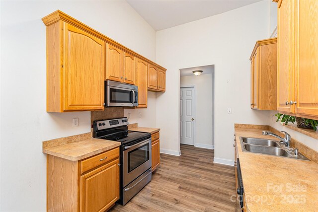 kitchen featuring stainless steel appliances, a sink, light countertops, light wood-type flooring, and baseboards