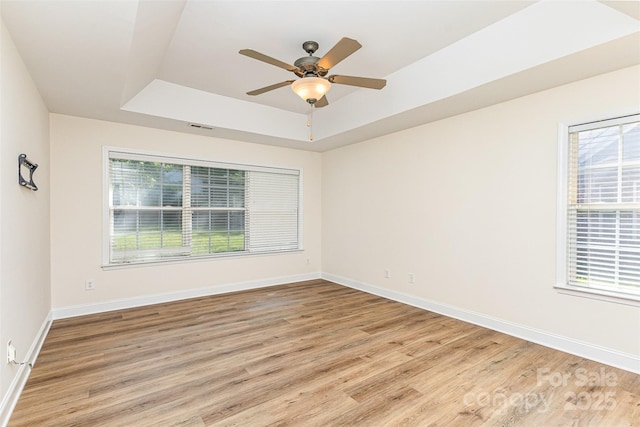 unfurnished room with a tray ceiling, light wood finished floors, baseboards, and ceiling fan