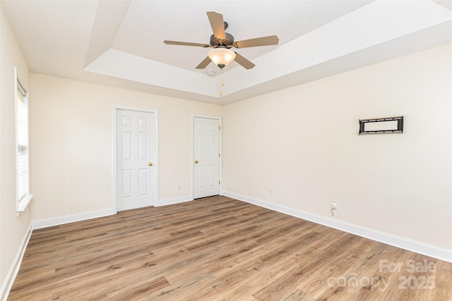 spare room featuring light wood-style floors, baseboards, a tray ceiling, and a ceiling fan