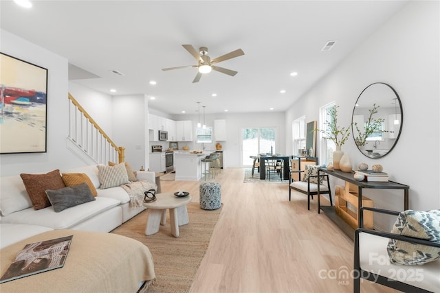 living room with ceiling fan, light wood-style flooring, recessed lighting, visible vents, and stairway