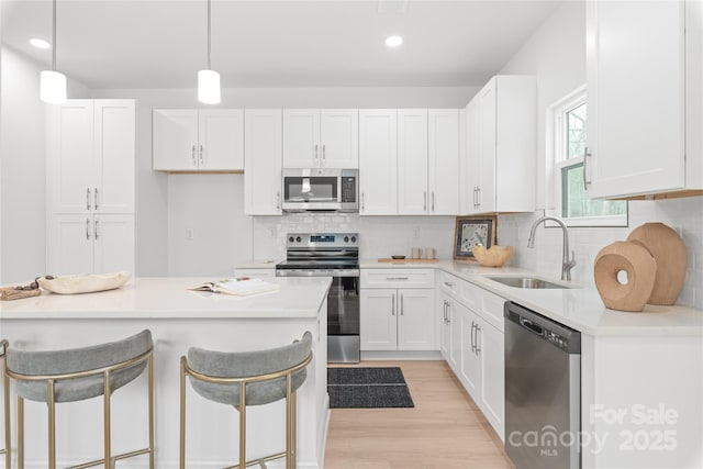 kitchen featuring a breakfast bar area, a sink, light wood finished floors, stainless steel appliances, and white cabinetry
