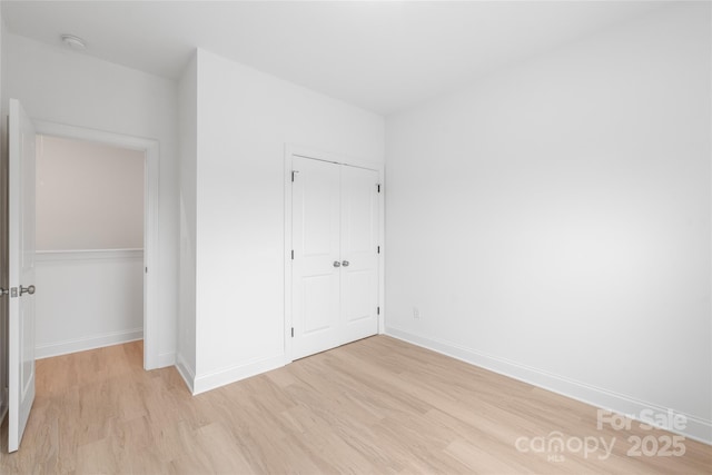 unfurnished bedroom featuring light wood-style floors, baseboards, and a closet