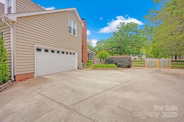view of side of home with concrete driveway, fence, an attached garage, and a chimney
