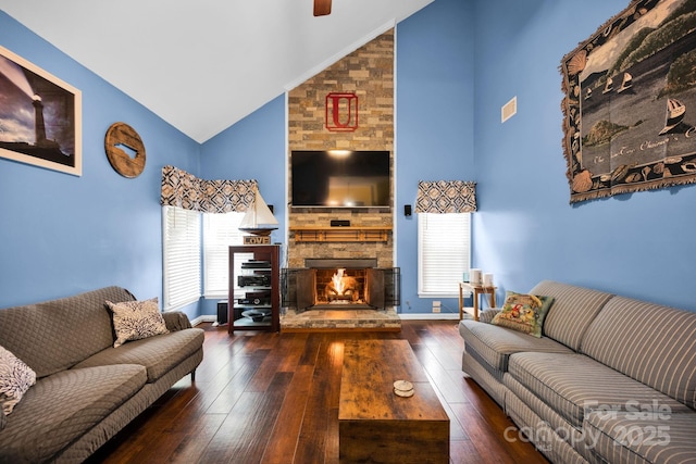 living area featuring high vaulted ceiling, hardwood / wood-style flooring, a stone fireplace, ceiling fan, and baseboards