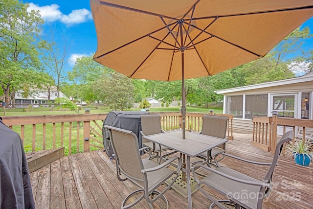 wooden terrace with outdoor dining area, a lawn, and a sunroom