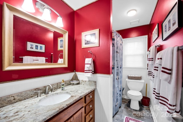 bathroom featuring a wainscoted wall, vanity, toilet, and a shower with shower curtain
