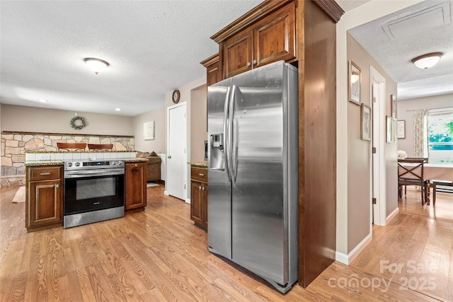 kitchen with baseboards, stainless steel appliances, light wood-type flooring, and a textured ceiling