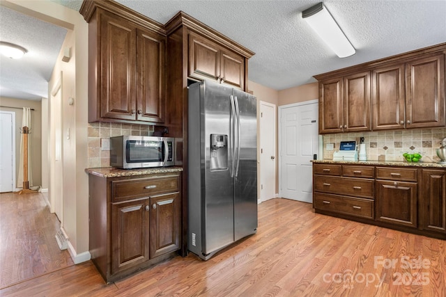 kitchen with light wood-style floors, a textured ceiling, appliances with stainless steel finishes, and backsplash