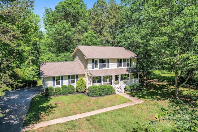 colonial-style house featuring covered porch, roof with shingles, driveway, and a front yard