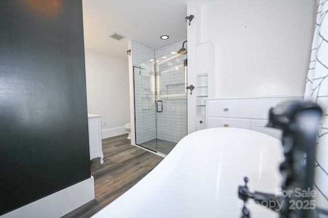 bathroom featuring a freestanding bath, toilet, wood finished floors, visible vents, and a stall shower