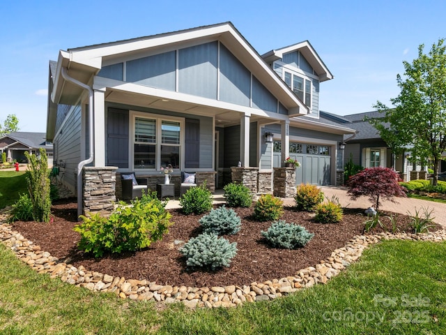 craftsman house featuring covered porch, driveway, and stone siding