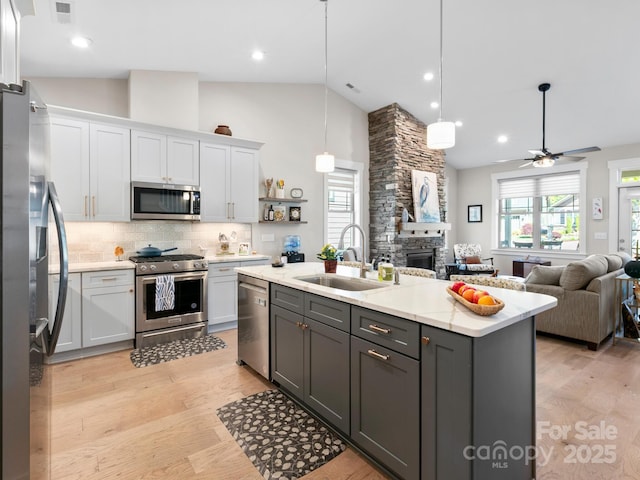 kitchen with stainless steel appliances, a sink, white cabinets, open floor plan, and high vaulted ceiling